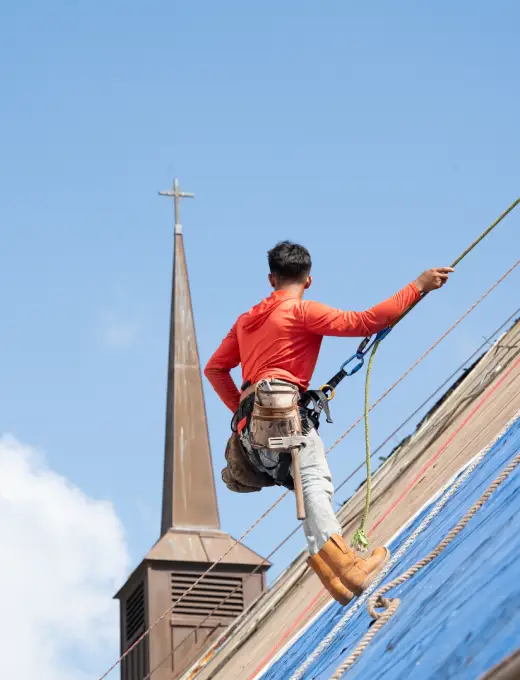 A worker wearing a safety harness rappels down a steep roof