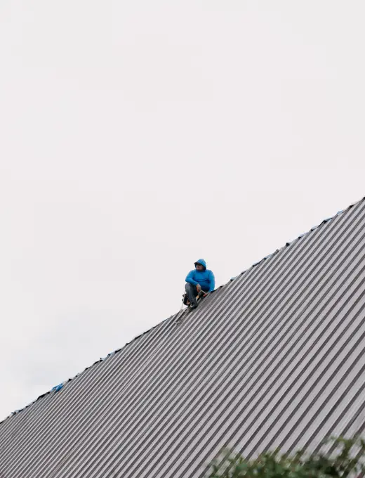 A person in a blue hoodie sits atop a steep metal roof