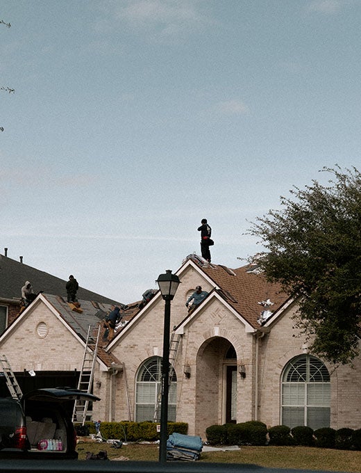 A roofer wearing a safety harness works on a steep, blue-covered roof